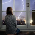 Mädchen sitzt vor dem Fenster und schaut auf Gewitter