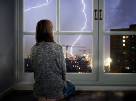 Mädchen sitzt vor dem Fenster und schaut auf Gewitter