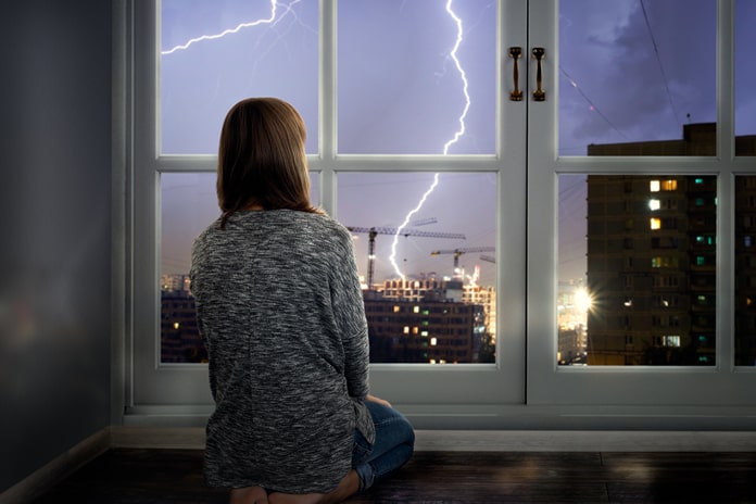 Mädchen sitzt vor dem Fenster und schaut auf Gewitter