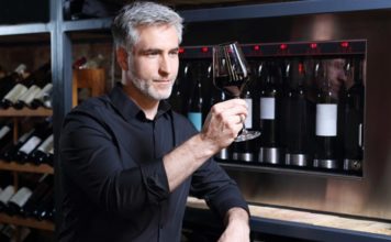 Mann mit Weinglas vor Weinkühlschrank