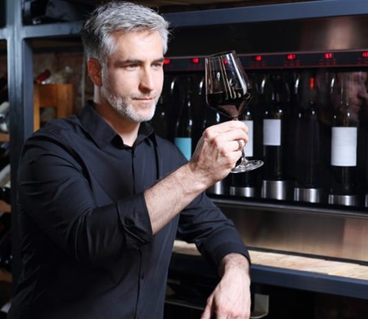 Mann mit Weinglas vor Weinkühlschrank