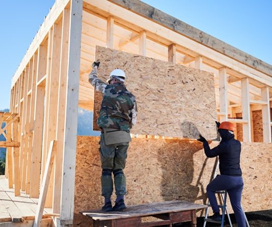 Holzmassivhaus oder Holzrahmenhaus? Unterschiede, Vor- und Nachteile Arbeiter befestigen eine Wand am Holzrahmenhaus